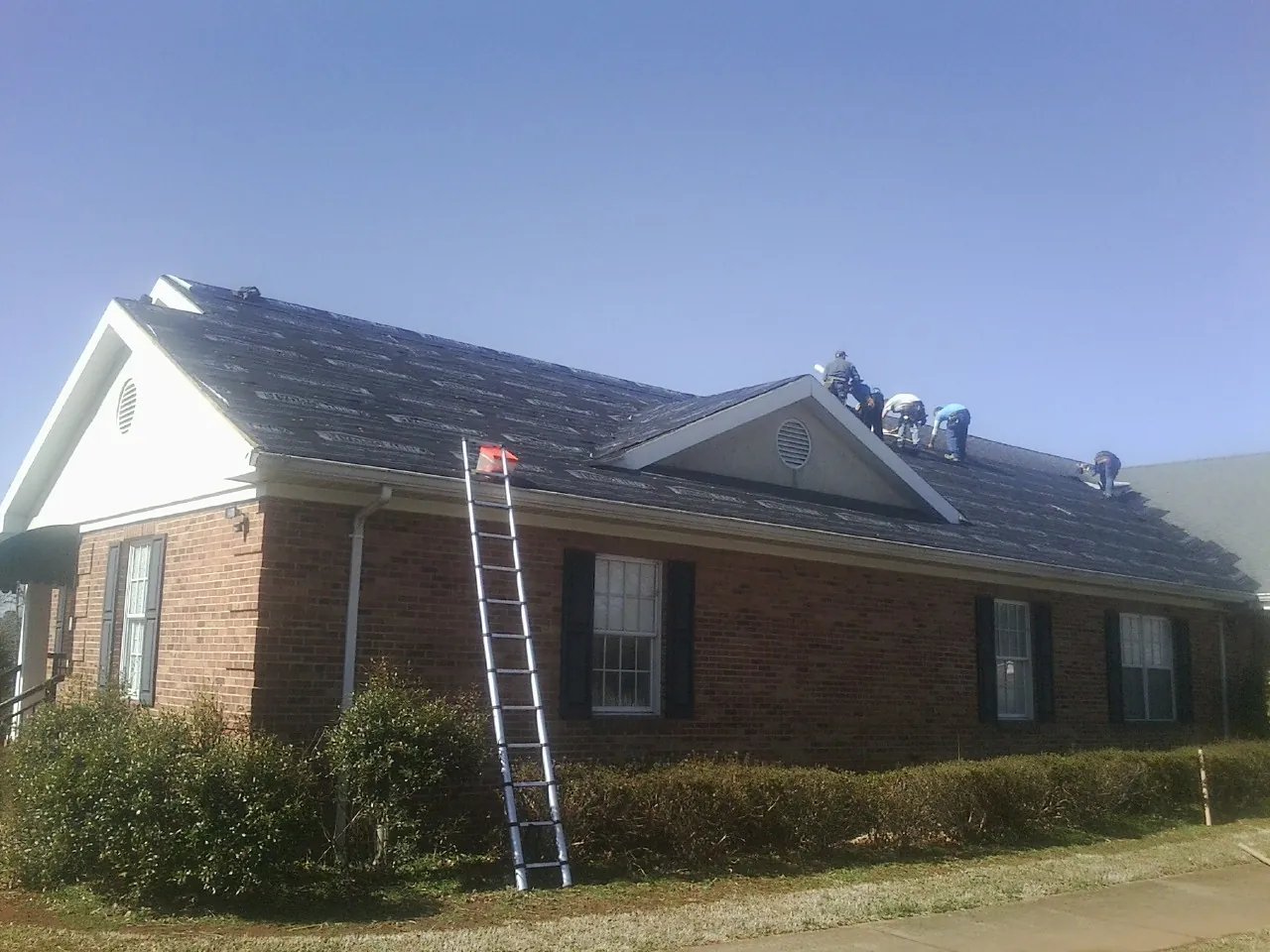 Crew tearing shingles off a brick ranch roof with a ladder set — Emergency Roof Repair work by our crew in Greer