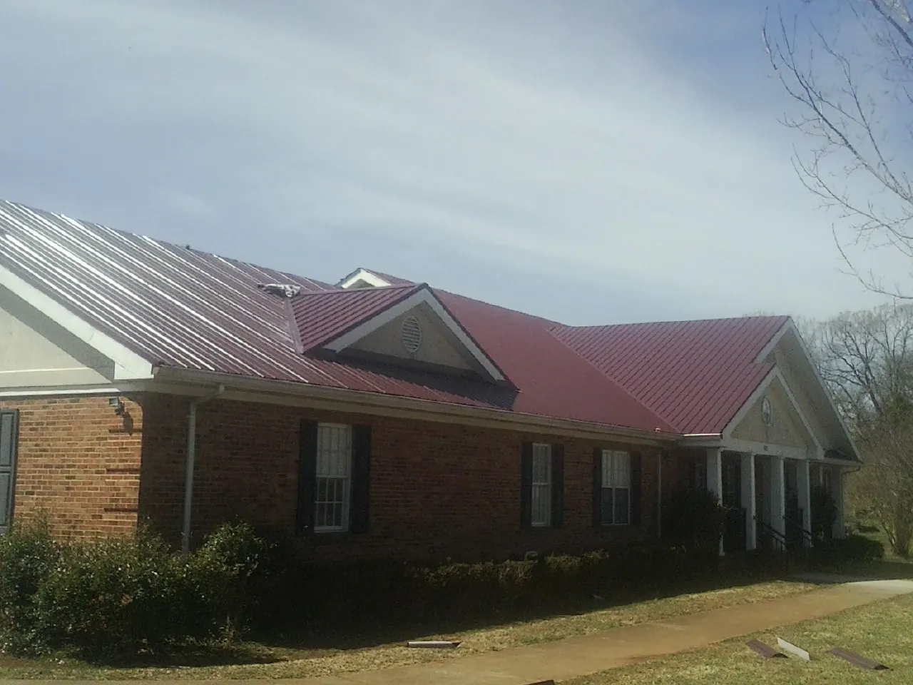 Red metal roof with gabled entries on a long brick building, from a Hail Damage Roof Repair job in Greer