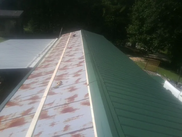 Old rusted panels beside newly installed green metal roofing — Wind Damage Roof Repair by Roofing Brothers in Greer
