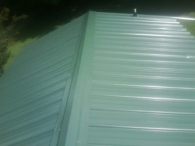 New green metal panels meeting at the ridge of a roof — Flat Roof Repair work by our crew in Greer
