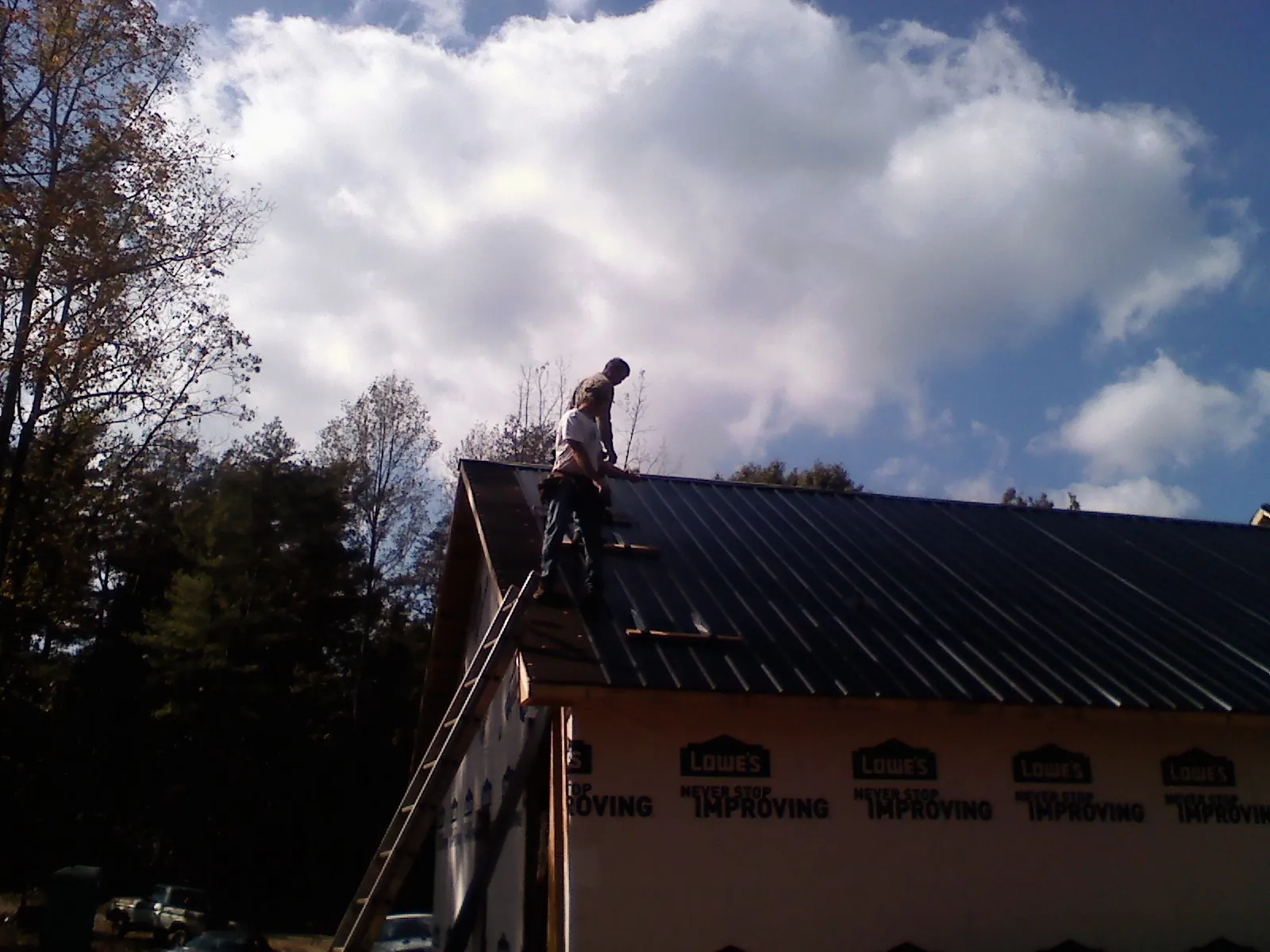 Roofer fastening dark metal panels high against a cloudy sky, from a Roof Inspection job in Greer